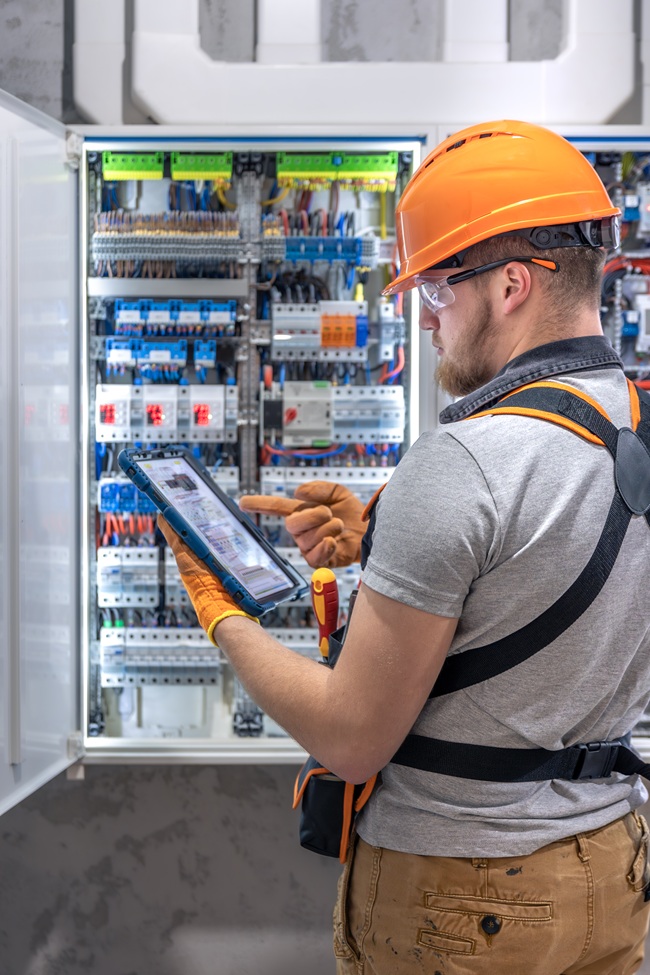 Male Electrician Overalls Focused Work Switchboard With Fuses Using Tablet